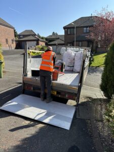 Premier Logs delivering onto a local driveway in Bolton. Small Premier Logs van with log bags on the back of it, with the tail lift down, showing the driver unloading logs on a sack truck.